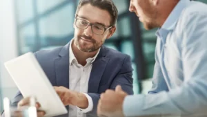 Asesor corporativo mostrando métricas en una tablet a un dueño de negocio, representando la asesoría y acompañamiento continuo después de abrir una empresa.