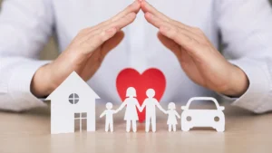 Manos en forma de techo protegiendo figuras de papel de una familia, una casa, un auto y un corazón, ilustrando la cobertura de seguros familiares.